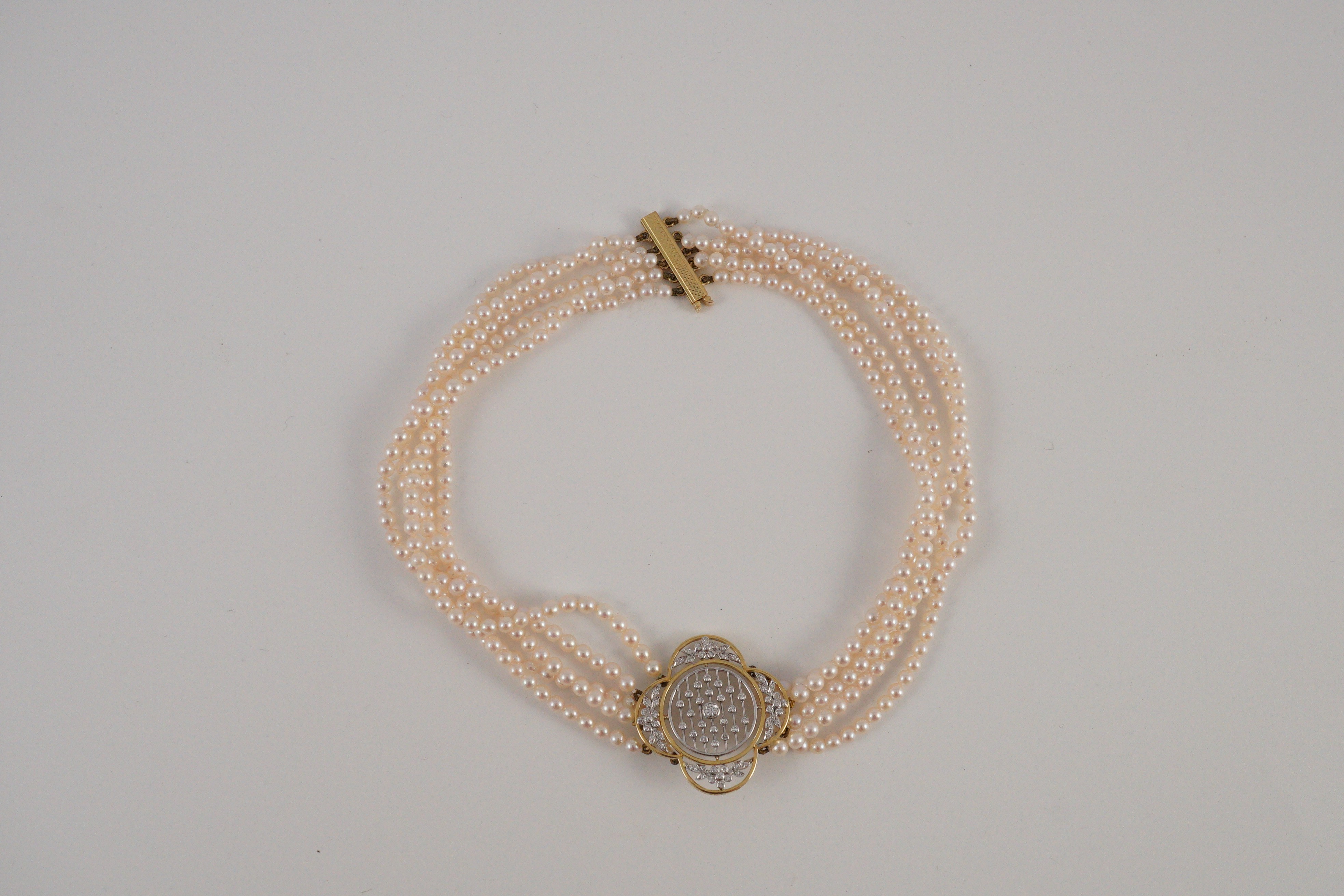 A quintuple strand seed pearl choker necklace, with pierced gold, platinum and diamond cluster set quatrefoil shaped clasp